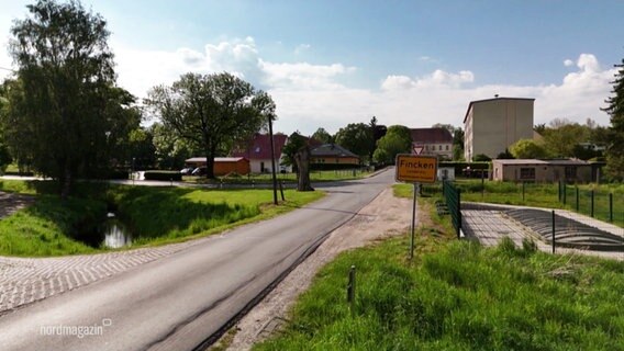 An einer kleinen Straße steht das Ortsschild von Fincken. © Screenshot 