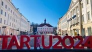 Ein mit weißen Fähnchen geschmückter Marktplatz auf dem ein roter Schriftzug steht "Tartu 2024". © Linnéa Kviske NDR 