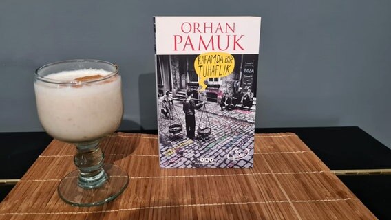 Ein Buch von Orhan Pamuk steht neben einem Glas türkischem Boza mit Zimt bestreut - Bild zum Podcast eat READ sleep  Folge 28 Türkisches Boza mit David Safier © NDR Foto: Jan Ehler