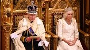 König Charles mit Krone sitzt neben Königin Camilla und liest im November 2023 bei der Regierungserklärung im Oberhaus des britischen Parlaments © dpa Foto: Leon Neal/PA Wire/dpa +++ dpa-Bildfunk +++